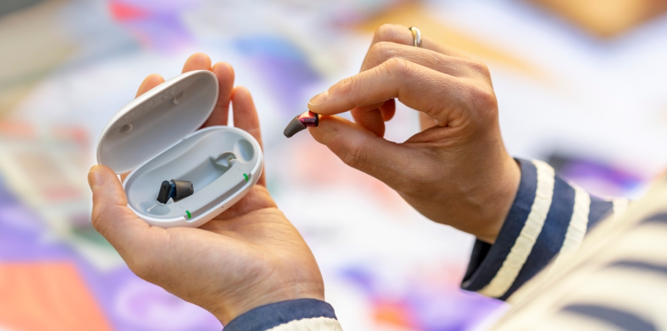 Main d'une femme plaçant un appareil auditif dans son boîtier de chargement.