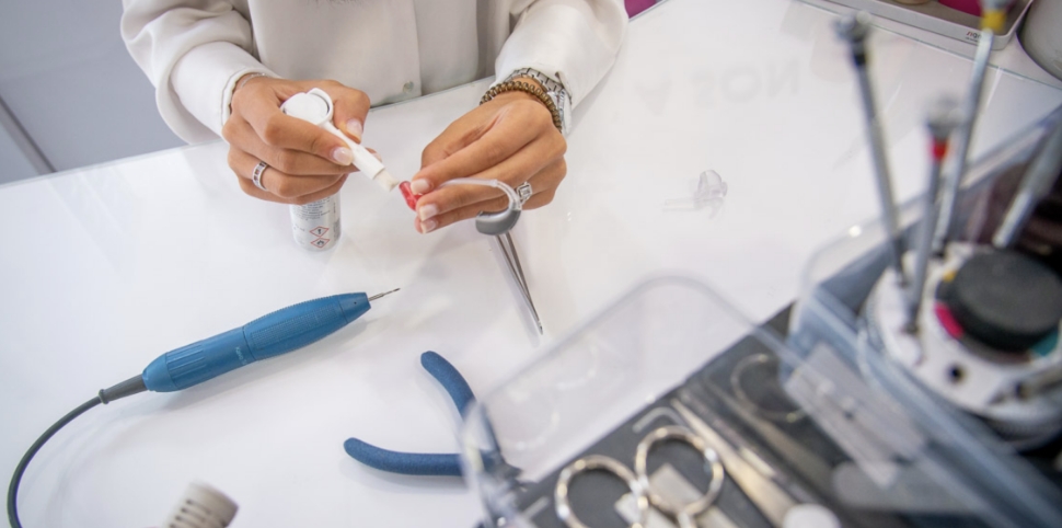 Mains d'un expert manipulant un appareil auditif avec des outils de précision.
